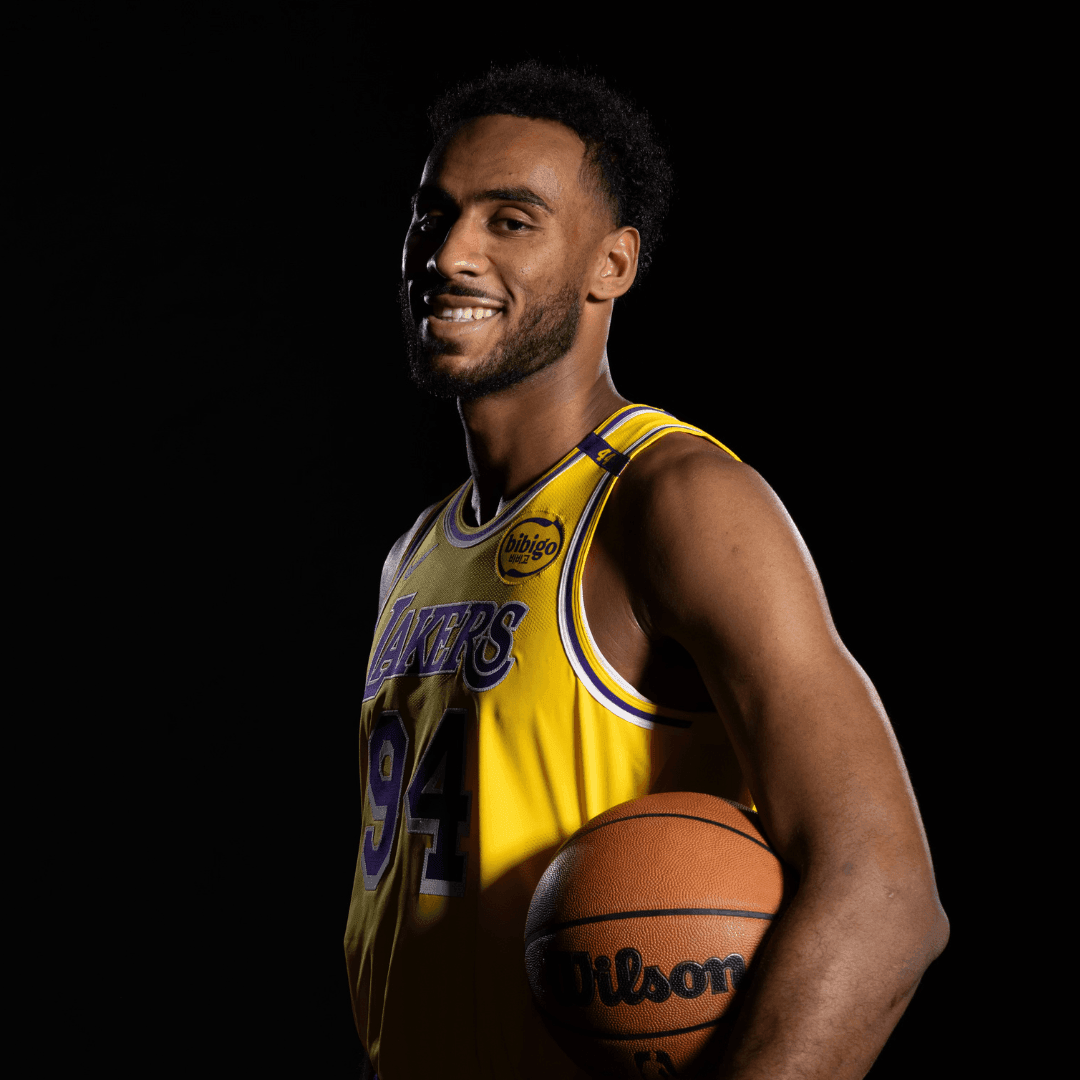 Basketball player in a yellow Lakers jersey holding a Wilson basketball, standing against a black background.